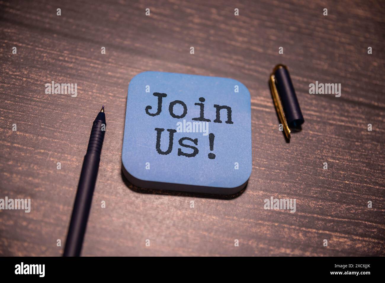 Das Konzept, das im Text „JOIN US“ auf einem Blatt vor einem mehrfarbigen Hintergrund vermittelt wird, deutet auf eine Einladung oder einen Aufruf hin, Teil von etwas zu sein. IT-Einflussnahme Stockfoto