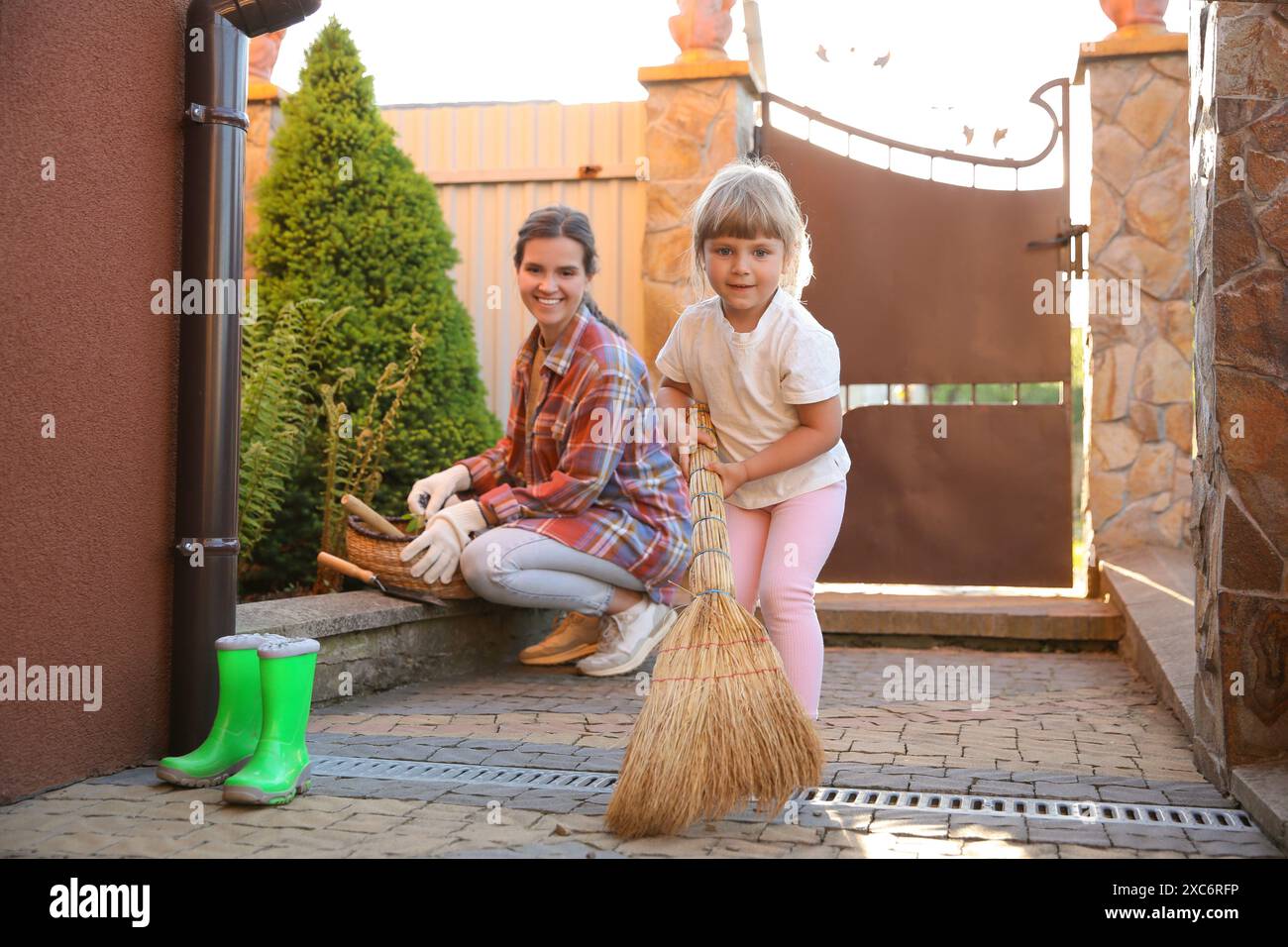 Mutter und ihre süße Tochter putzen zusammen in der Nähe des Hauses am Frühlingstag Stockfoto