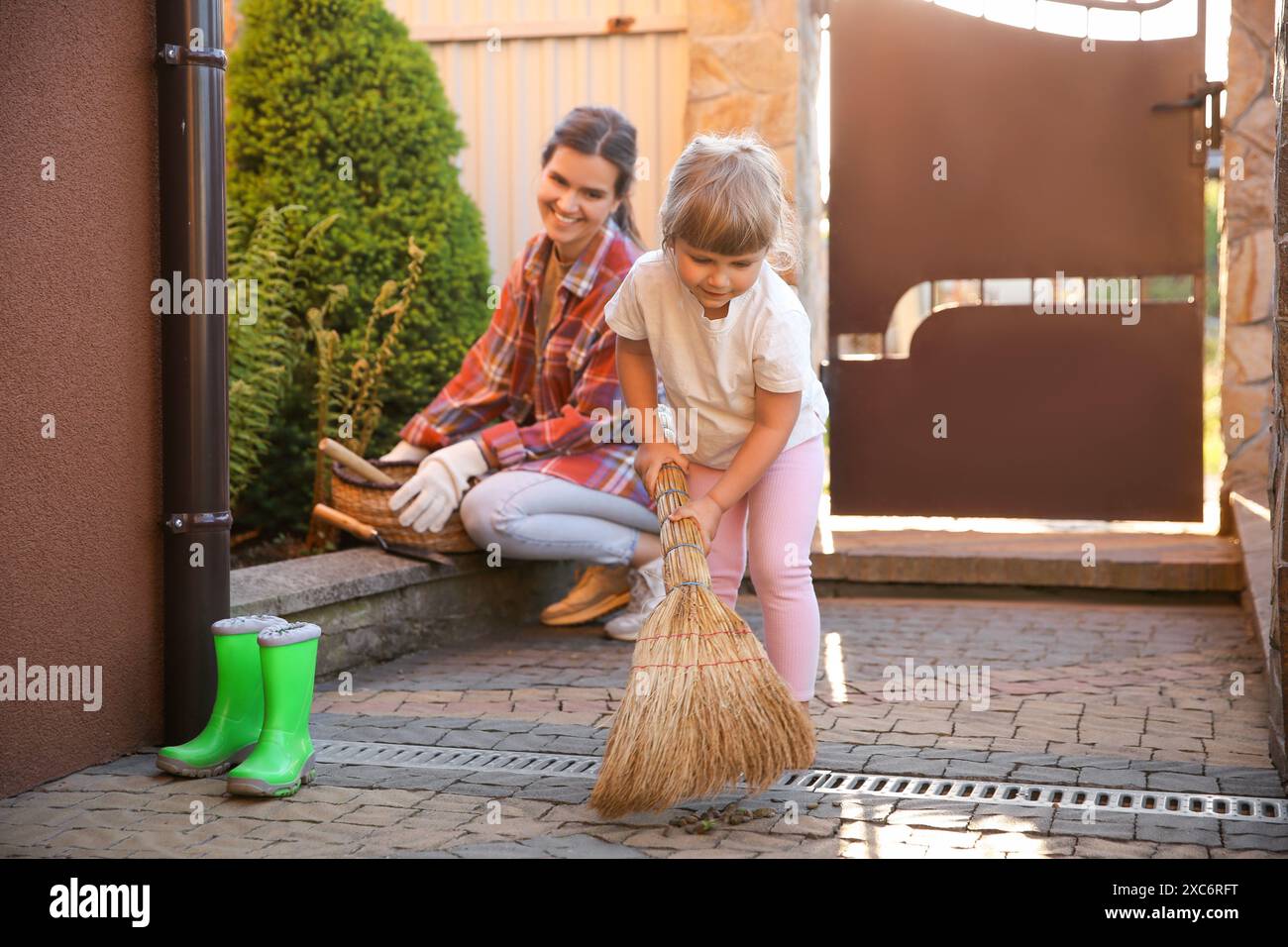 Mutter und ihre süße Tochter putzen zusammen in der Nähe des Hauses am Frühlingstag Stockfoto