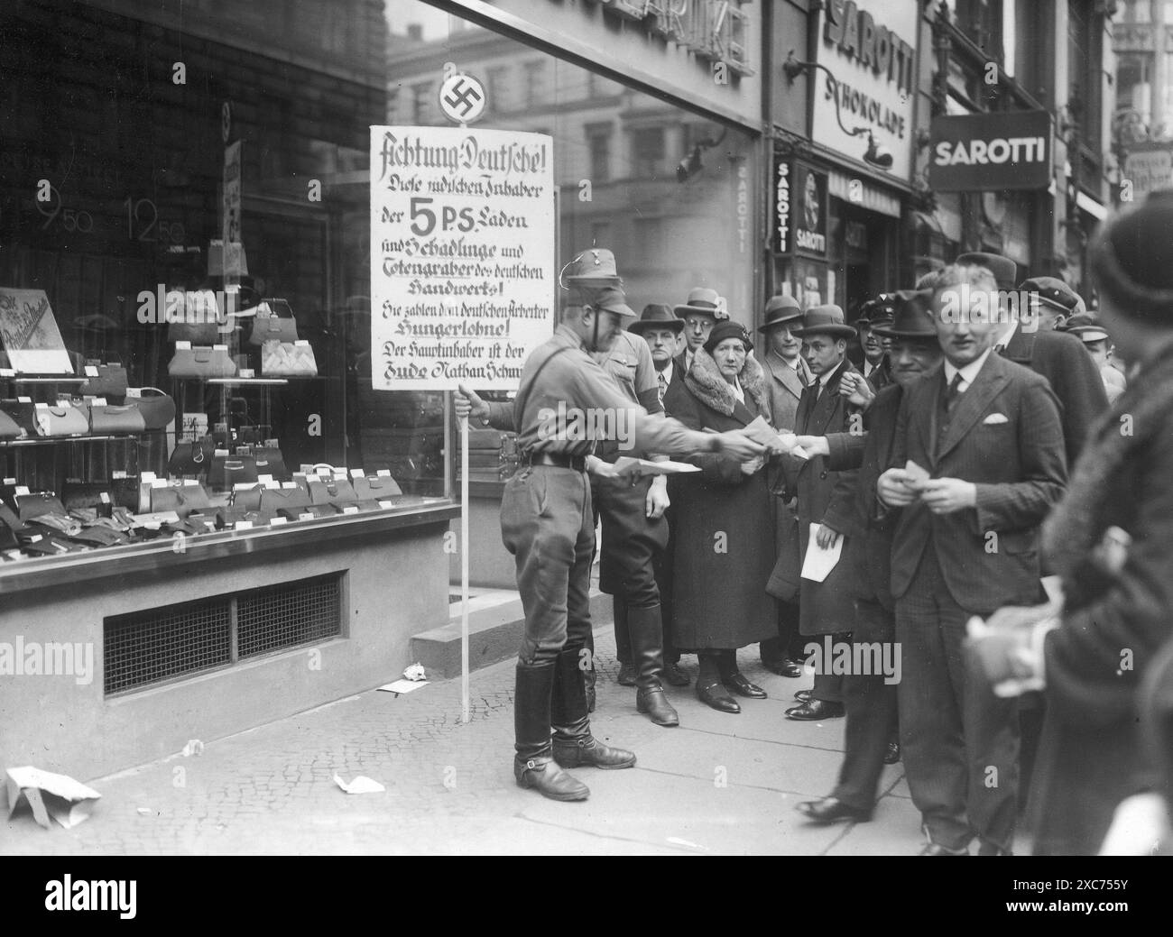 Mitglieder der Sturmabteilung (SA, die berüchtigten Brownshirts) während des Boykotts jüdischer Unternehmen vom 1. April 1933. Hier gibt es antisemitische Flugblätter in Berlin. Der Boykott jüdischer Unternehmen war die erste direkte antijüdische Aktion, die zum Ausschluss der Juden aus der Gesellschaft und schließlich zur Vernichtung führte und nur zwei Monate nach Hitlers Machtergreifung stattfand. Auf dem Schild steht: "Achtung, Deutsche! Diese jüdischen Besitzer der 5 P.S.-Geschäfte sind Parasiten und Bestattungskünstler deutscher Handwerkskunst! Sie zahlen Hungerlöhne an deutsche Arbeiter! Der Haupteigentümer ist der Stockfoto
