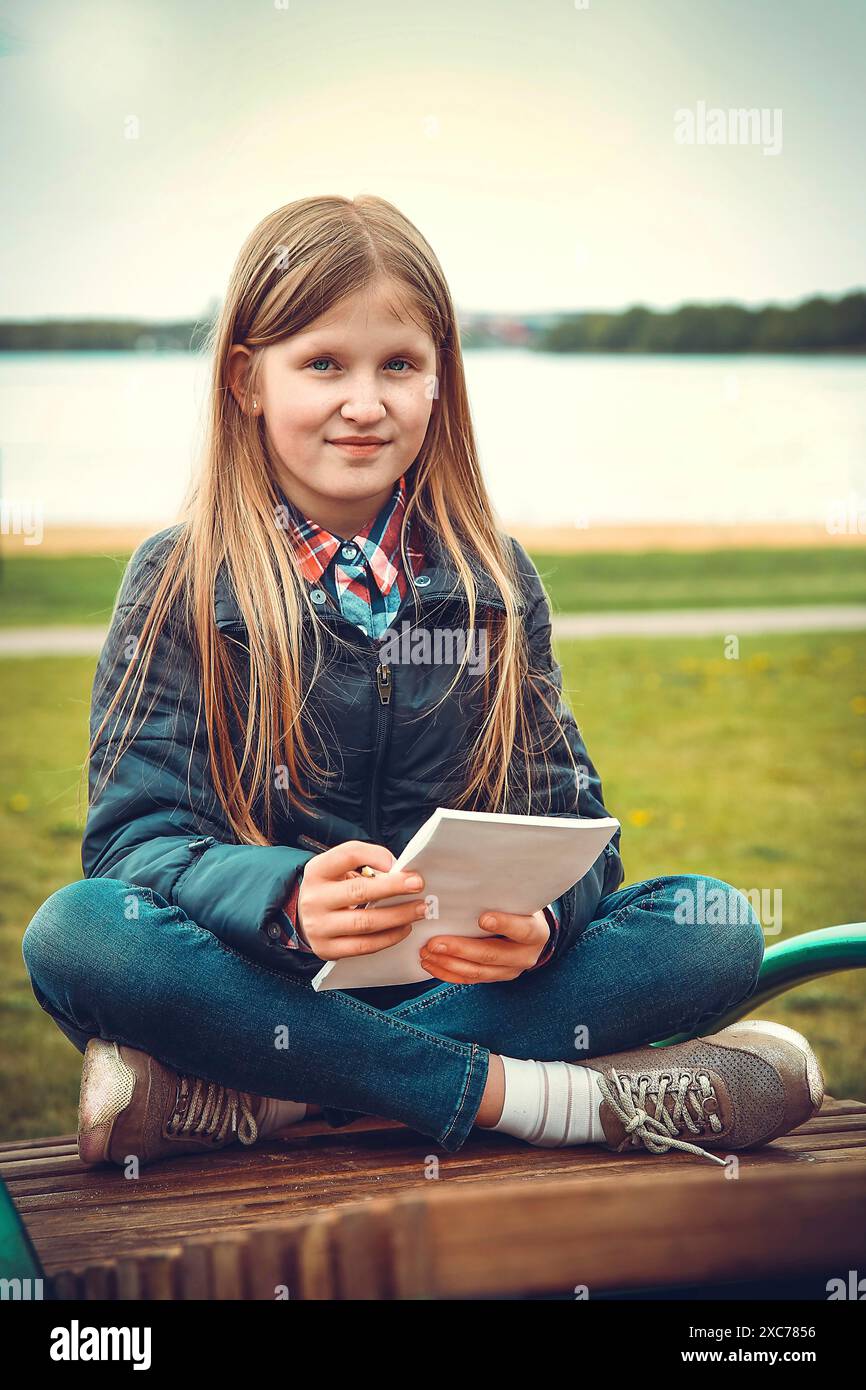 Ein junges Mädchen sitzt im Kreuz auf einer Bank in der Nähe eines Sees und hält ein Blatt Papier in der Hand, Weißrussland, Minsk Stockfoto