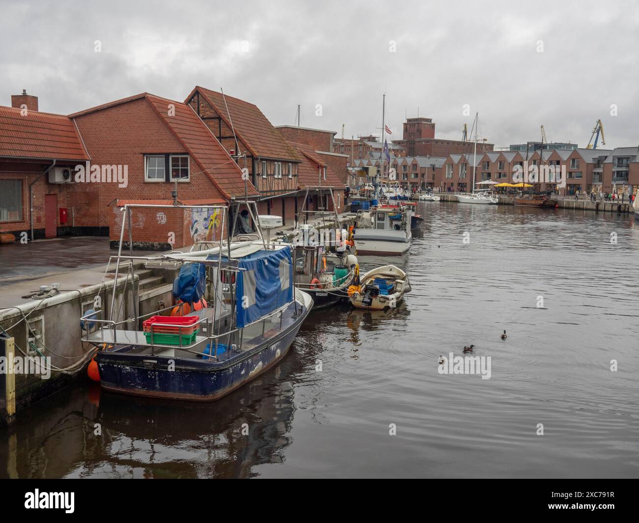 Hafen mit verankerten Booten entlang eines Kais, umgeben von Backsteinhäusern unter bewölktem Himmel, zingst, ostsee, deutschland Stockfoto