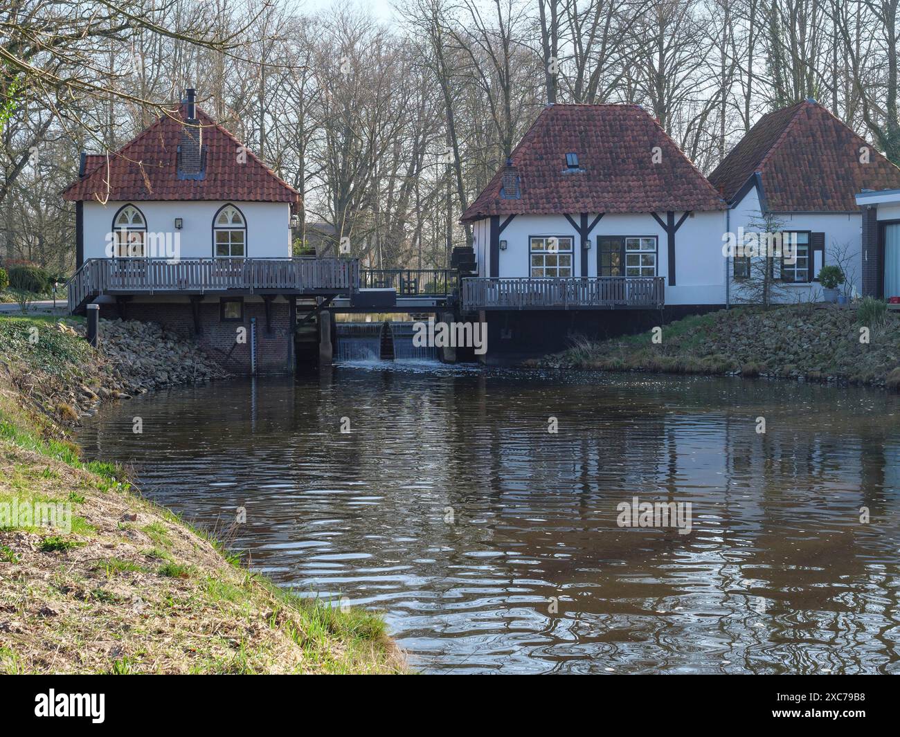 Zwei ältere Häuser am Fluss und ein kleiner Wasserfall, verbunden durch eine Brücke, umgeben von Wald, winterwswijk, gelderland, Niederlande Stockfoto