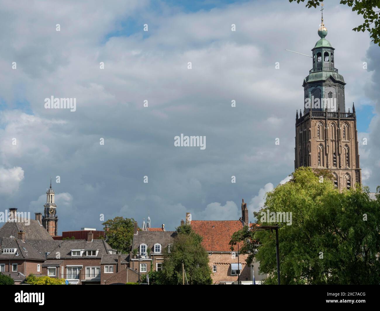 Ein hoher Kirchturm ragt über den Dächern einer Stadt unter bewölktem Himmel, umgeben von grünen Bäumen, zutphen, gelderland, niederlande Stockfoto