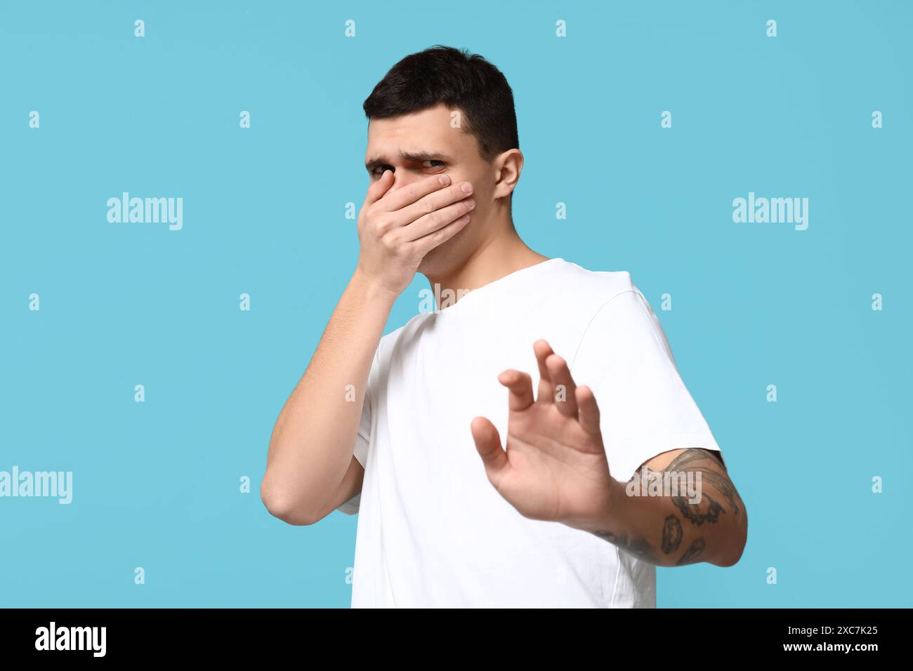 Schöner junger Mann, der einen schlechten Geruch auf blauem Hintergrund hat Stockfoto