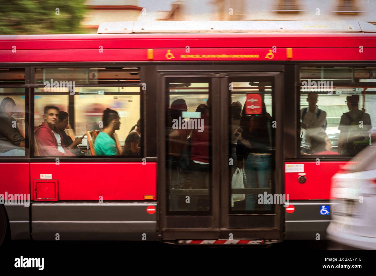 Roter Stadtbus in Sevilla, España mit verschiedenen Pendlern. Städtische öffentliche Verkehrsmittel, die das tägliche Leben zeigen. Stockfoto