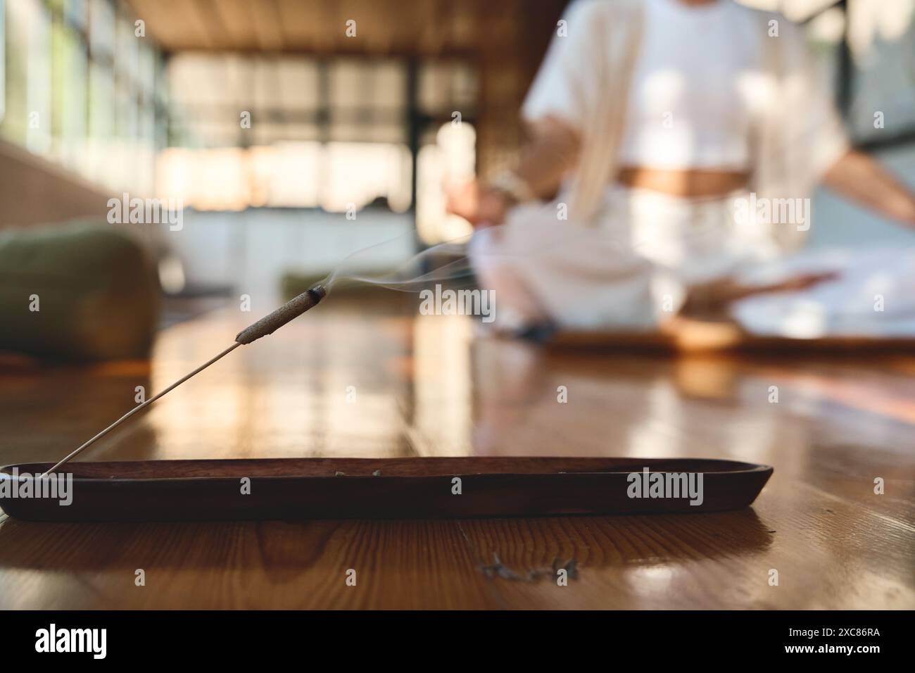 Räucherstäbchen mit Rauch auf Holzhalter mit meditierender Person auf Hintergrund. Stockfoto
