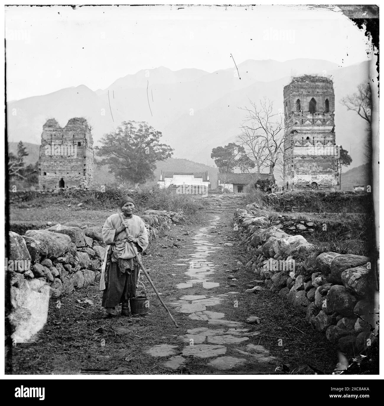 Dieses Foto, das John Thomson 1872 aufgenommen hat, zeigt die Ruinen von Taiping Kung, einem religiösen Gebäude in der Nähe von Kiukiang in der Provinz Kiangsi, China. Eine Einzelfigur, möglicherweise ein Einheimischer, steht auf einem Steinweg, der in Richtung des baufälligen Bauwerks führt. Das Bild bietet einen Einblick in die Vergangenheit und zeigt die Überreste eines einst großen Gebäudes inmitten der sanften Hügel des ländlichen Chinas. Stockfoto Dieses Foto, das John Thomson 1872 aufgenommen hat, zeigt die Ruinen von Taiping Kung, einem religiösen Gebäude in der Nähe von Kiukiang in der Provinz Kiangsi, China. Eine Einzelfigur, möglicherweise ein Einheimischer, steht auf einem Steinweg, der in Richtung des baufälligen Bauwerks führt. Das Bild bietet einen Einblick in die Vergangenheit und zeigt die Überreste eines einst großen Gebäudes inmitten der sanften Hügel des ländlichen Chinas. Stockfoto