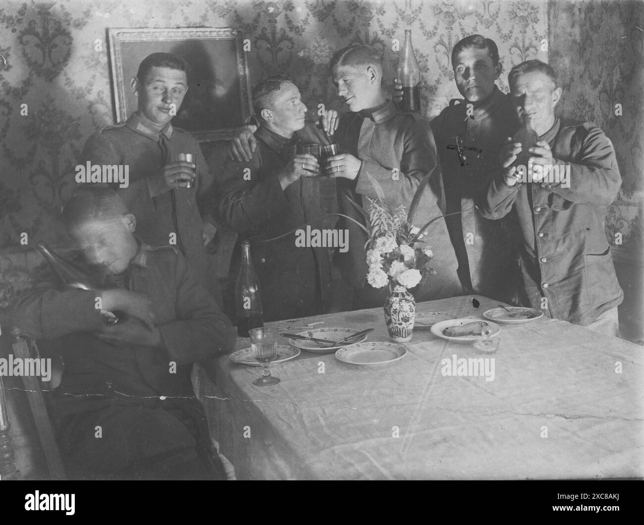 Ein Schwarzweiß-Foto, das eine Gruppe von sechs deutschen Soldaten in einem Speisesaal zeigt, wahrscheinlich während des Ersten Weltkriegs oder früher gefangen genommen. Die Soldaten sitzen an einem Tisch, unterhalten sich zwanglos und genießen Drinks. Stockfoto