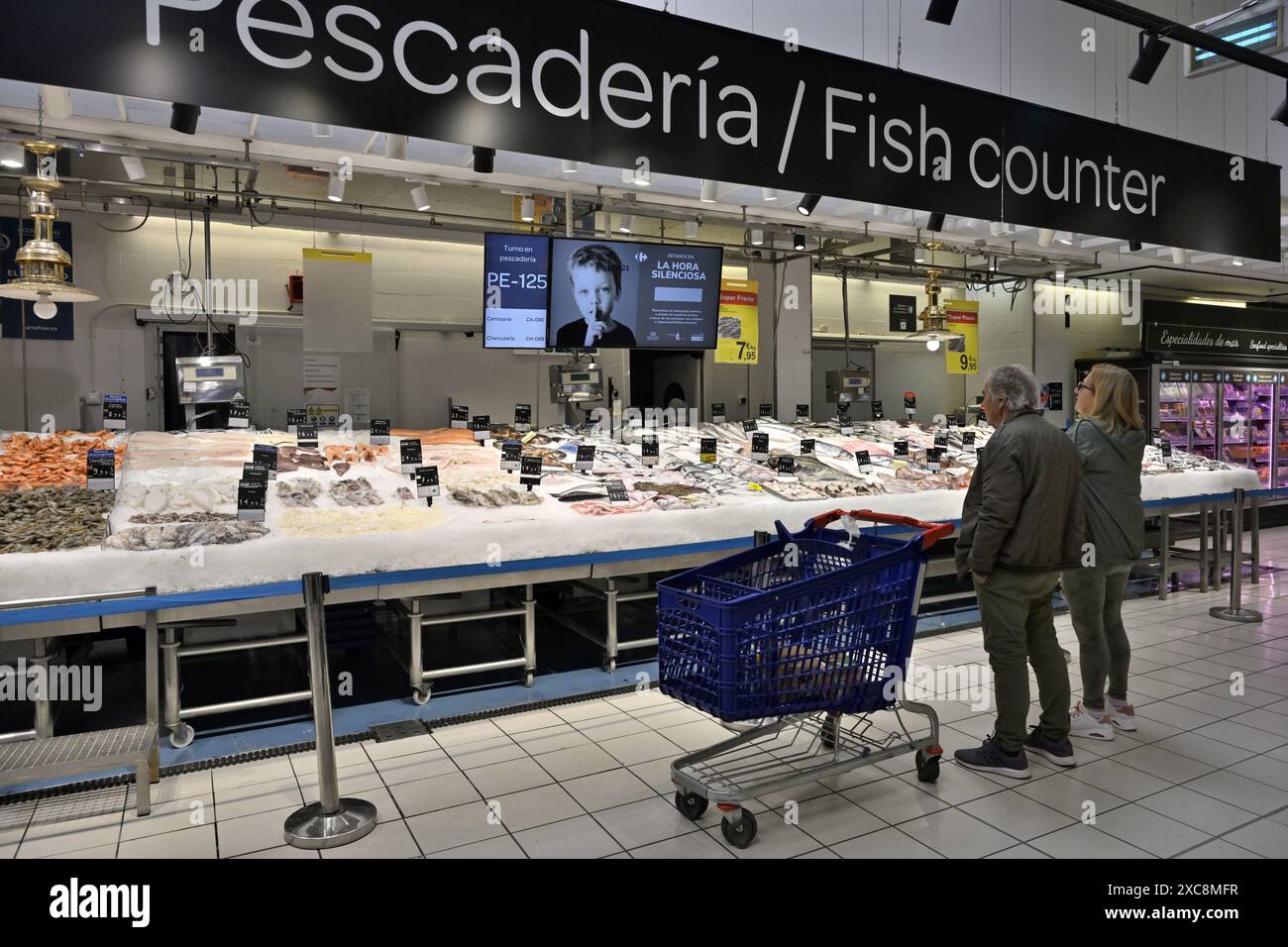 Fischtheke im Supermarkt Carrefour, Spanien, mit Kunden vor Ort, die sich das große Angebot an Fisch ansehen Stockfoto