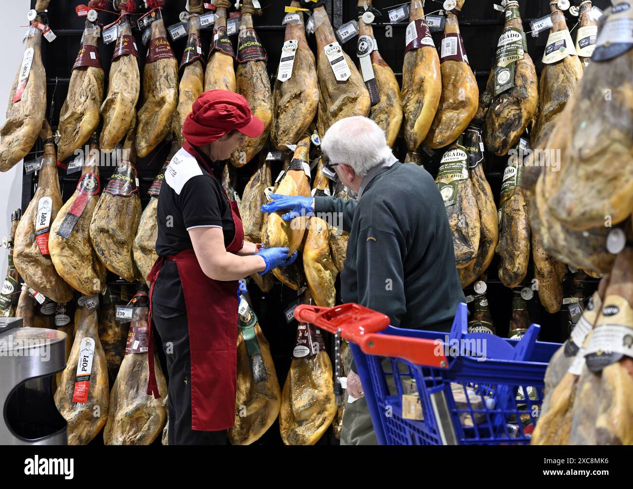 Mitarbeiter und Kunden untersuchen die Schinkenstücke, die im Supermarkt Carrefour, Spanien, verkauft werden Stockfoto