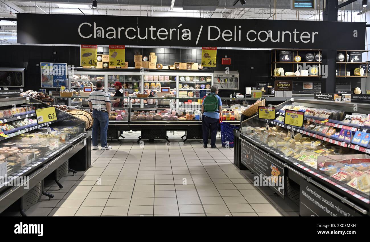 Feinkosttheke im Supermarkt Carrefour, Spanien, mit Kunden vor Ort, die sich das breite Angebot an Käse und Fleisch ansehen Stockfoto