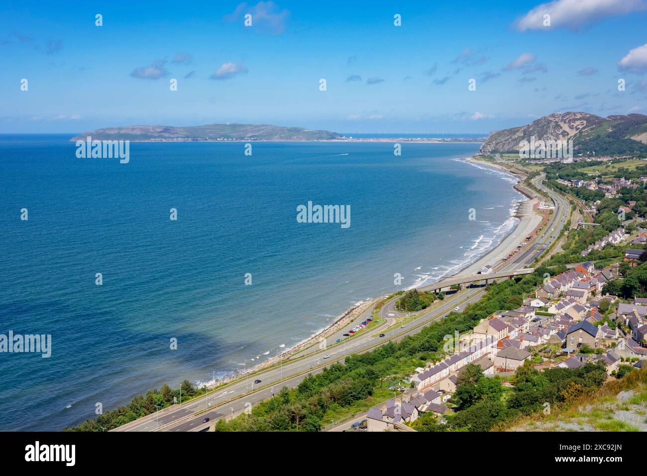 Hohe Aussicht auf Dorf, Strand und A55 Expressway Straße an der Küste mit Great Orme in der Ferne. Penmaenmawr, Conwy, Nordwales, Großbritannien Stockfoto