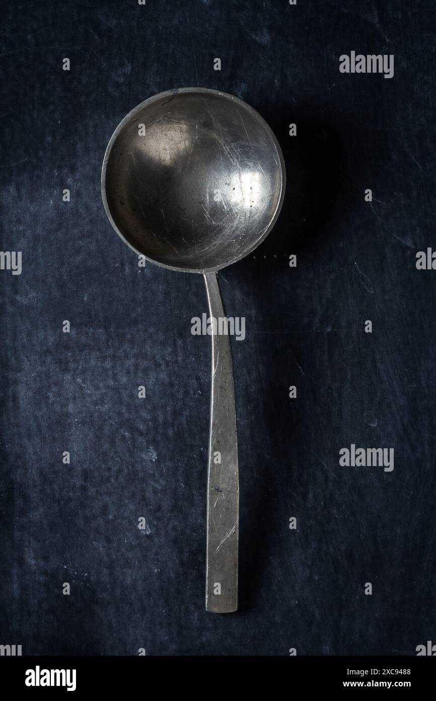 Großer, alter, leerer Löffel auf schwarzem Hintergrund. Flach verlegt. Draufsicht. Speisekonzept. Dunkle Stimmungsfotografie. Stockfoto