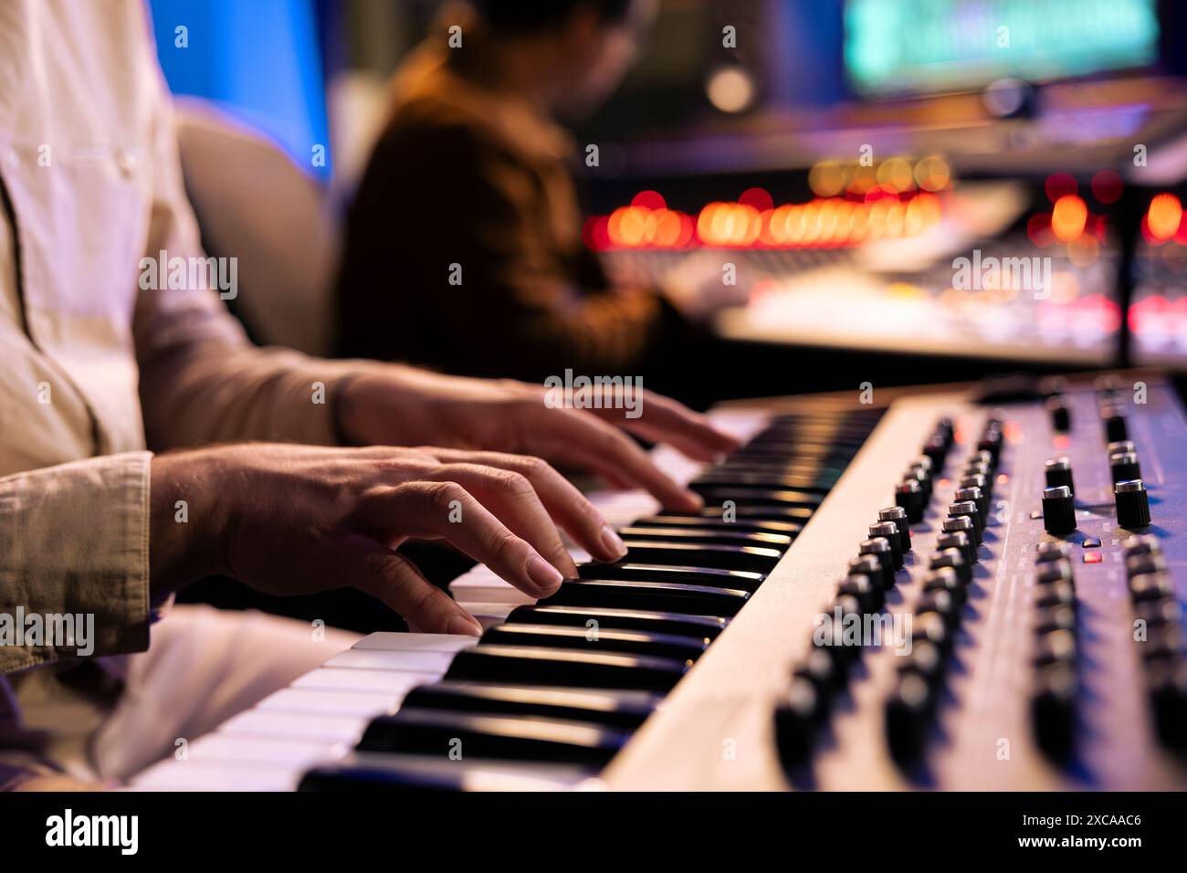 Künstler, der sein Lied auf elektronischem Keyboard Piano aufnimmt, mit Toningenieur im professionellen Studio arbeitet und neue Musik produziert. Sänger komponiert auf Synthesizer. Nahaufnahme. Stockfoto