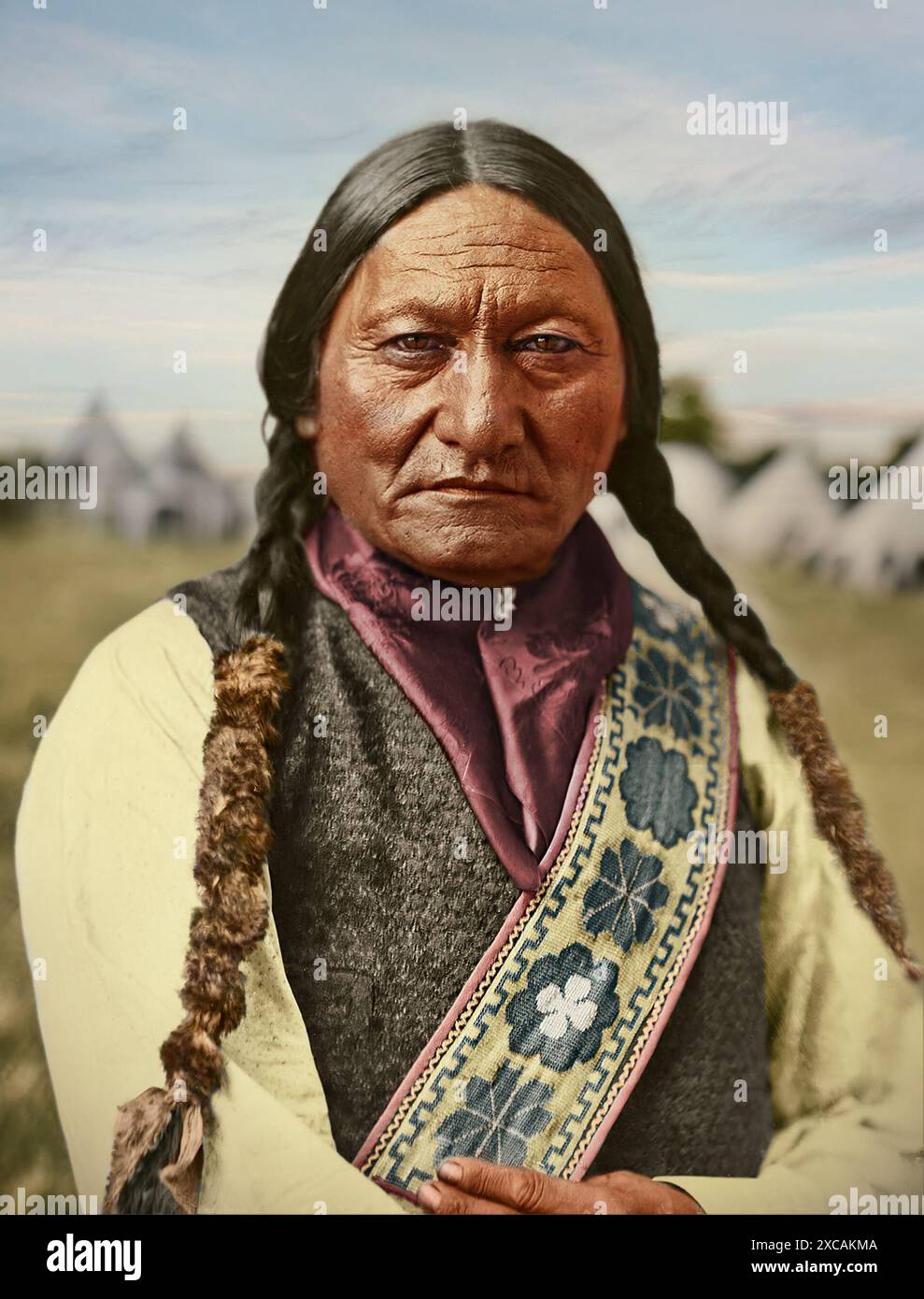 Ein detailliertes Porträt eines indigenen Führers in traditioneller Kleidung. Das Bild zeigt das kulturelle Erbe, die Geschichte und die Stärke vor dem Hintergrund historischer Wohnhäuser. Sitting Bull (ca. 1831–1890), geborene Tatanka Iyotake, war ein Häuptling der Hunkpapa Lakota, der für seinen Widerstand gegen die US-Expansionspolitik bekannt war. Er führte die Oceti Sakowin (Sioux) Stämme in ihrem Kampf gegen Siedler auf den nördlichen Great Plains. Er half dabei, die US-Truppen 1876 in der Schlacht am Little Big Horn zu besiegen. Er bleibt ein Symbol der traditionellen Sioux-Werte und des Widerstands Stockfoto