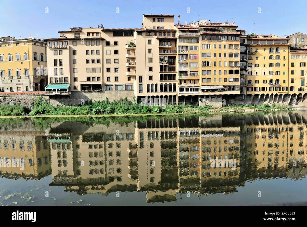 Mehrere Häuserreihen stehen entlang eines Flusses (Arno) ihre Reflexionen sind im Wasser zu sehen, an einem klaren Tag, Florenz, Toskana, Italien Stockfoto