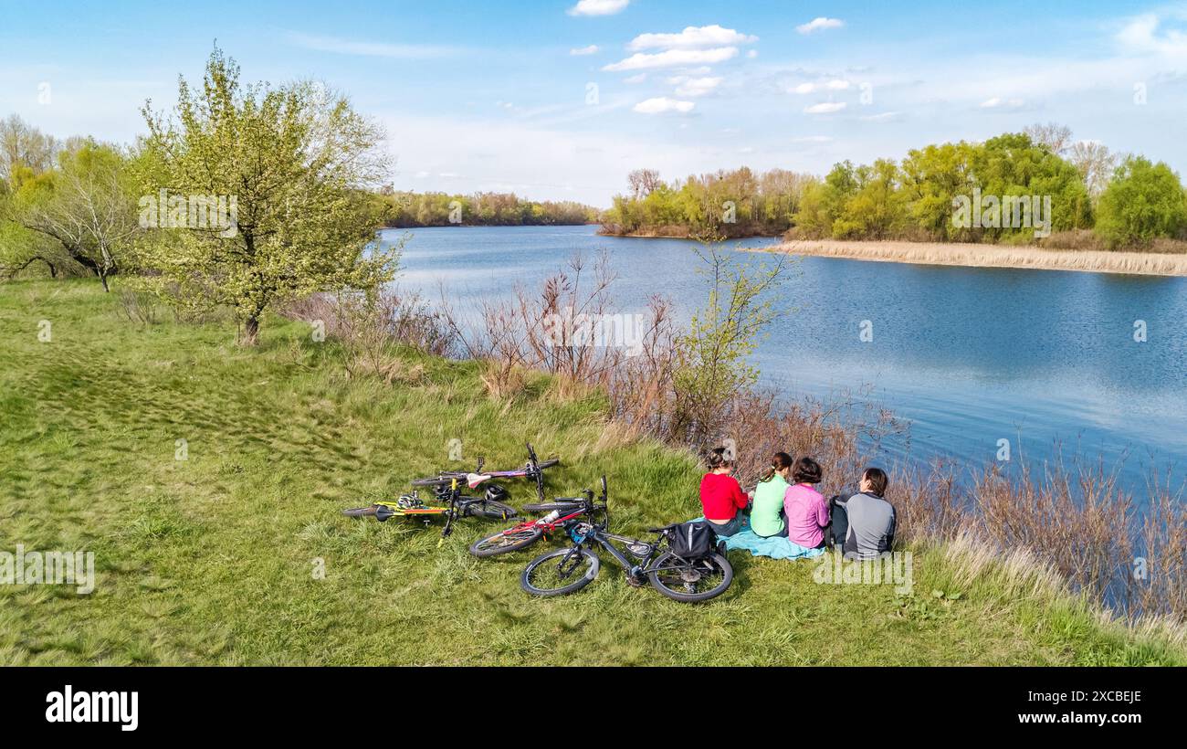 Familie auf Fahrrädern im Freien, aktive Eltern und Kinder auf Fahrrädern, aus der Vogelperspektive auf glückliche Familie mit Kindern, die sich in der Nähe des wunderschönen Flusses entspannen Stockfoto