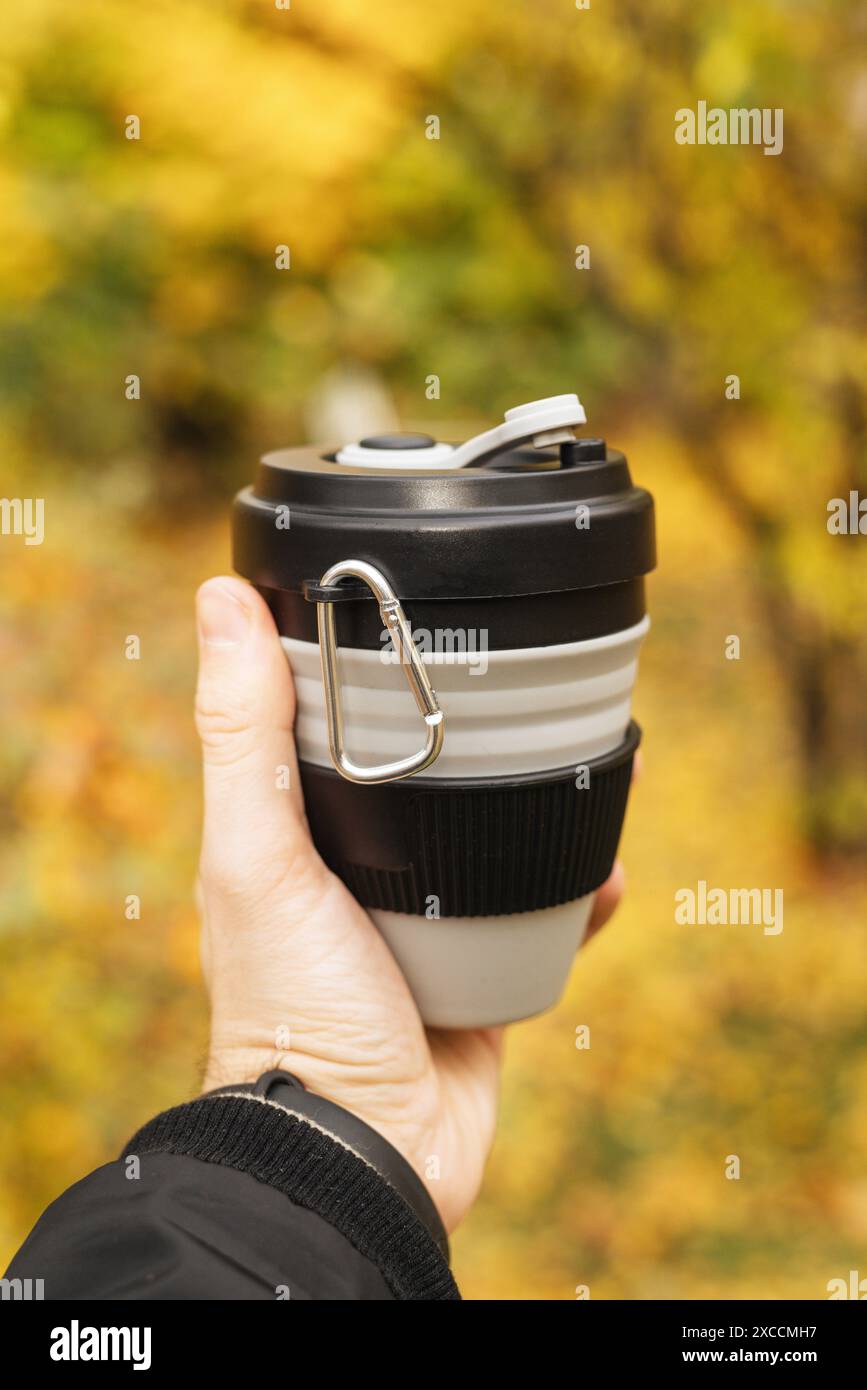 Wiederverwendbarer stylischer schwarzer Becher in den Händen eines Mannes, Nahaufnahme, umweltfreundlicher, handlicher Becher ohne Abfall, kein Kunststoffkonzept. Stockfoto