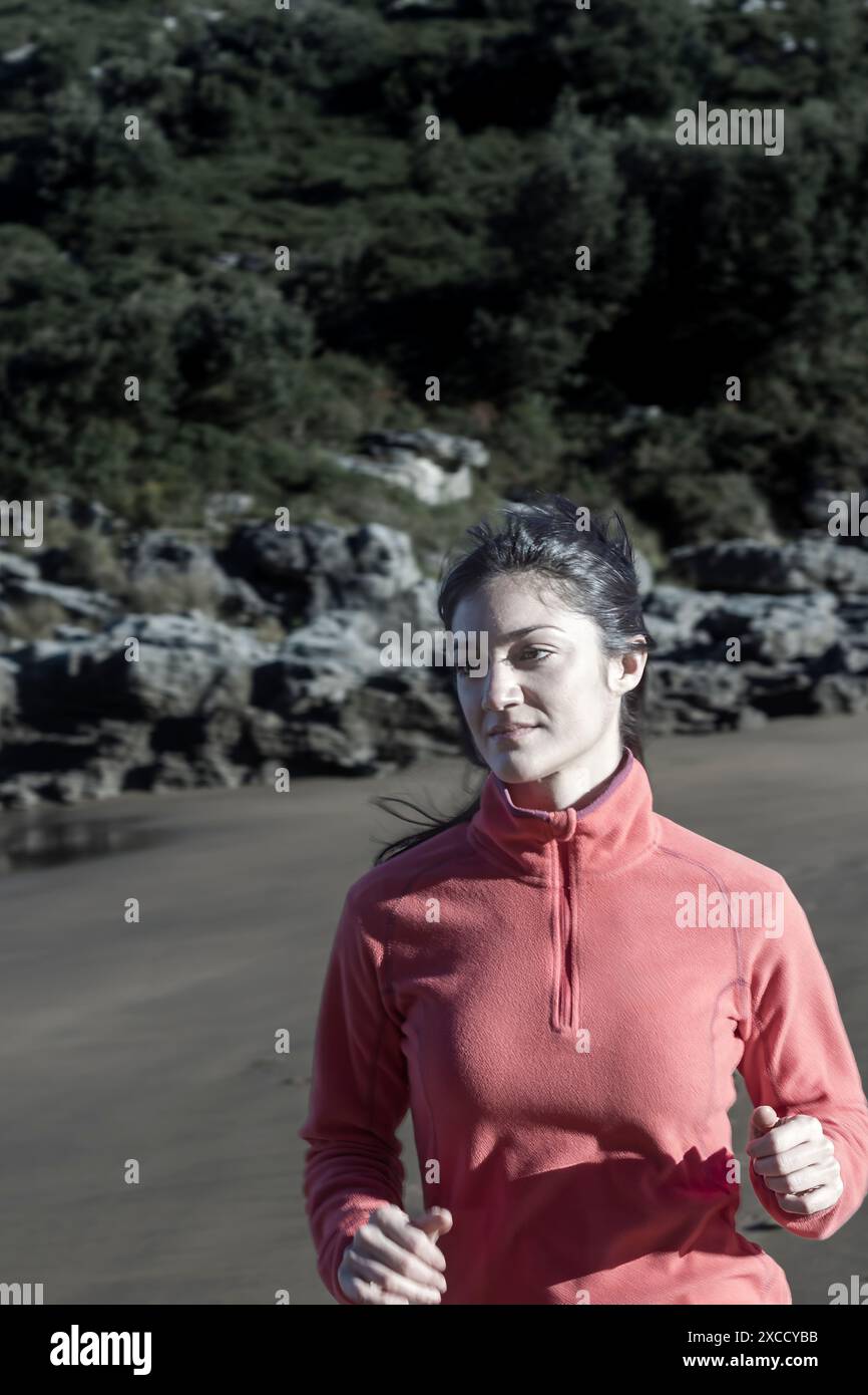 Frau, die am Strand in einer rosa Fleecejacke joggt. Fitness- und Fitnesskonzept im Freien Stockfoto