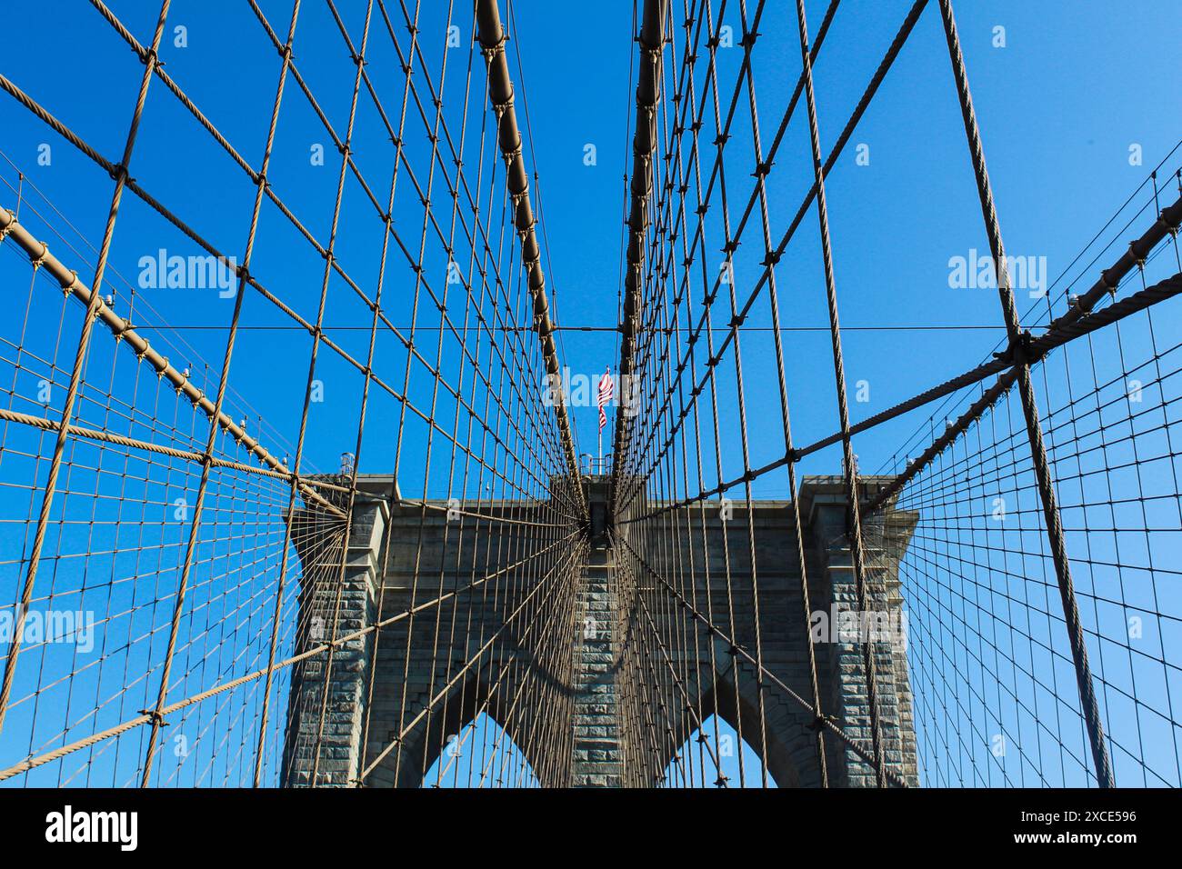 15.03.2022, New York, Nahaufnahme der architektonischen Bögen der Brooklyn Bridge, mit der ikonischen amerikanischen Flagge, die stolz im Wind flattert Stockfoto