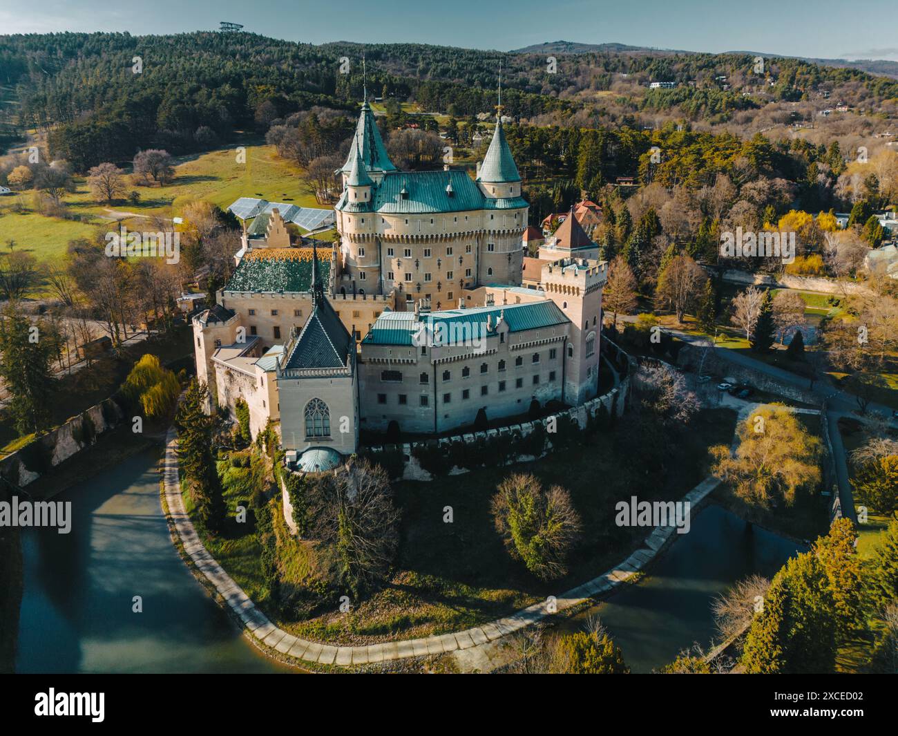 Panoramablick aus der Vogelperspektive auf das Schloss Bojnice in der Slowakei. Malerische Landschaft mit berühmtem Palast und historischer Festung des UNESCO-Weltkulturerbes zwischen Bäumen des Parks, der Straße und dem tiefen Wassergraben Stockfoto