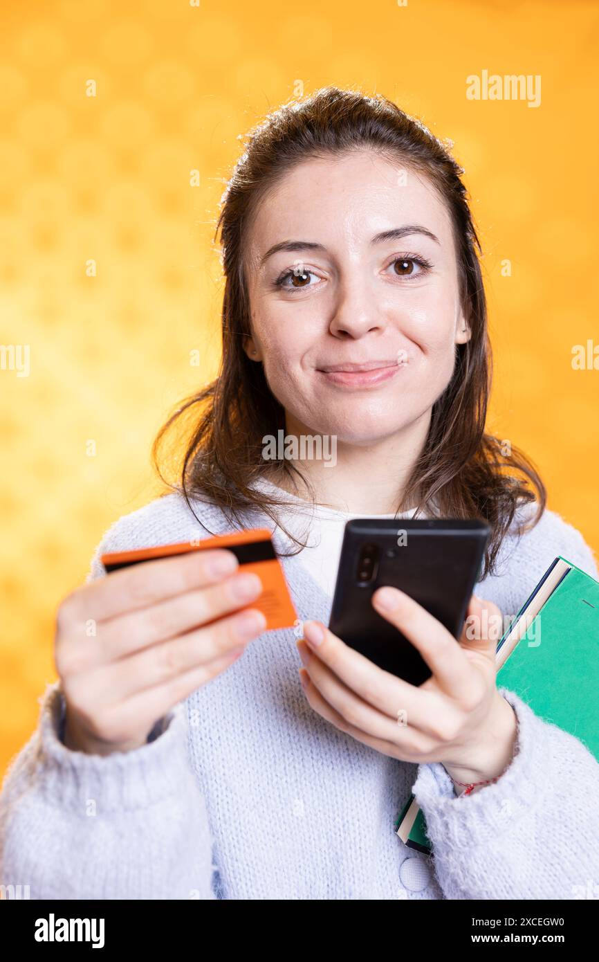 Frau mit einem Stapel Bücher in der Hand, die begeistert ist, mehr mit Kreditkarte zu kaufen, isoliert über Studiohintergrund. Bücherwurm, der einen Stapel Romane und ein Handy hält, kaufte Sachen zum Lesen Stockfoto