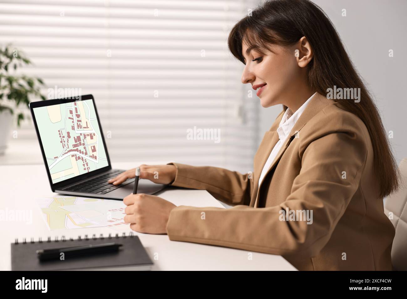 Frau, die mit Katasterkarte auf Laptop am Tisch im Büro arbeitet Stockfoto