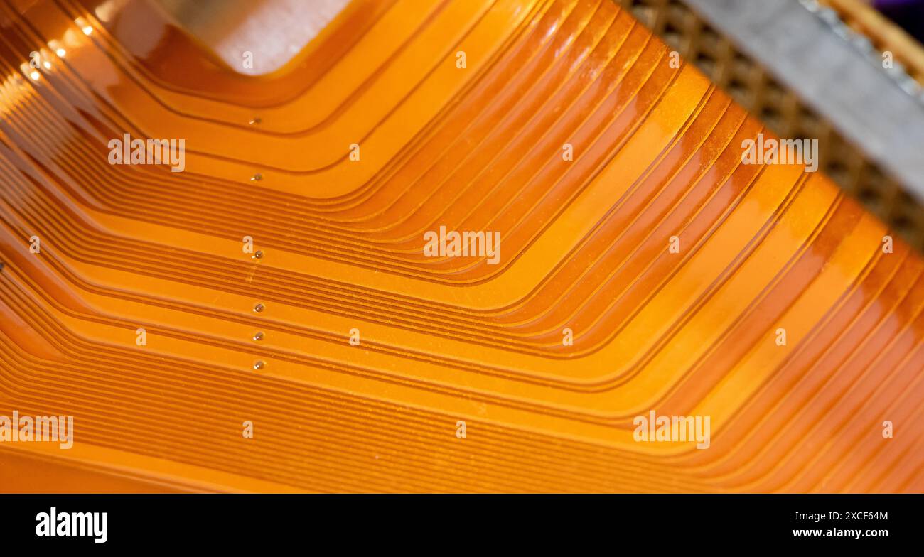 Eine detaillierte Nahaufnahme eines kupferfarbenen flexiblen Flachbandkabels mit parallelen leitenden Linien und einer Hintergrundstruktur mit abstrakter Technologie in warmoranger Farbe Stockfoto