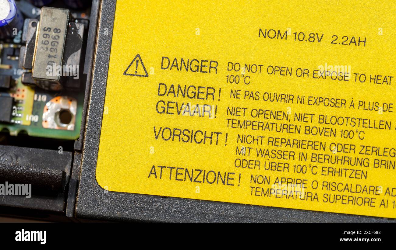 Ein gelbes Gefahrenetikett mit Warnhinweis zur Wärmeeinwirkung in verschiedenen Sprachen und ein Ausrufezeichen-Dreieck auf einem generischen Laptop-BA eines elektronischen Geräts Stockfoto