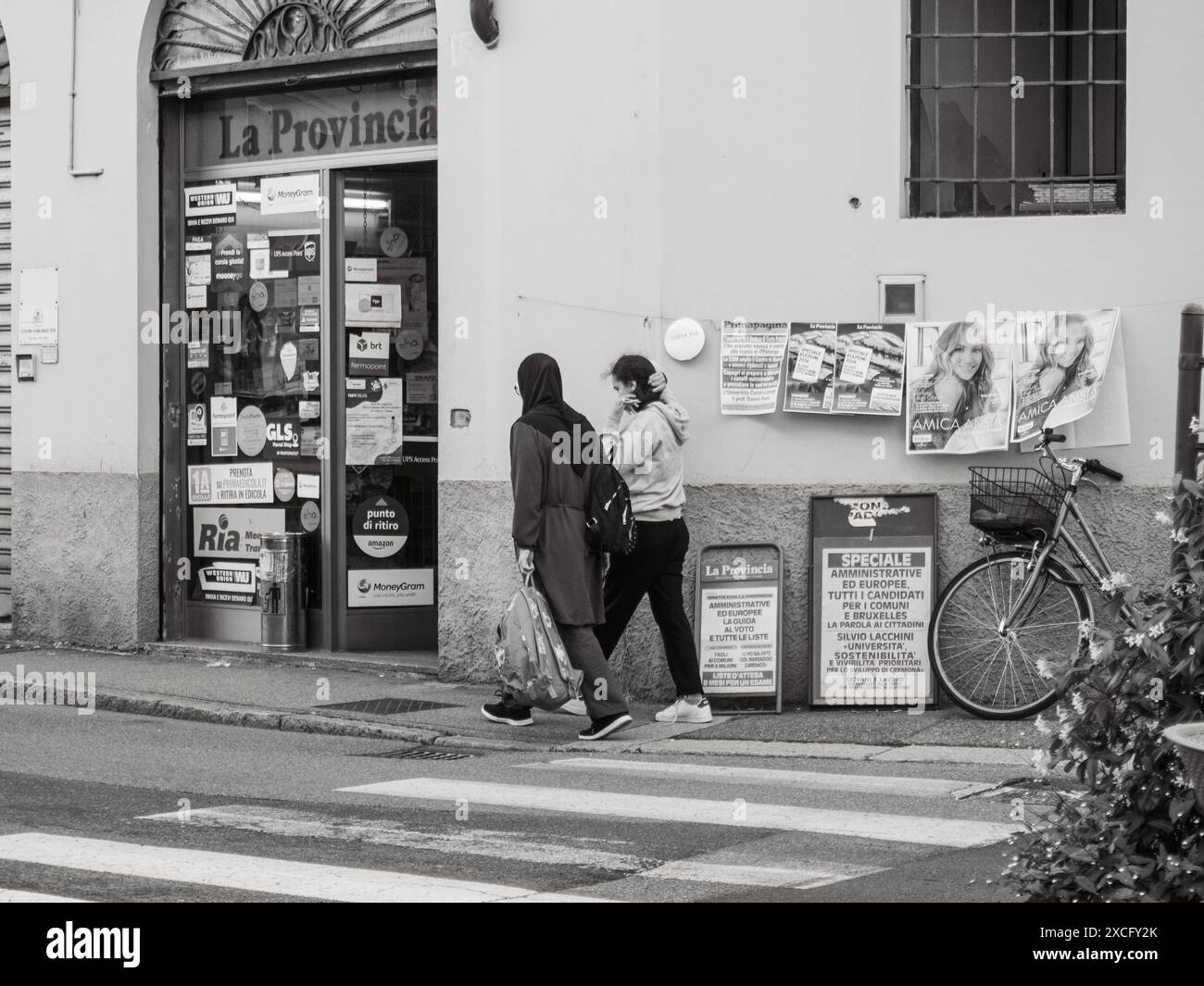 Cremona, Italien - 10. Juni 2024 zwei Frauen laufen an einer Ladenfront vorbei, die mit Plakaten und Anzeigen in Schwarz-weiß bedeckt ist Stockfoto