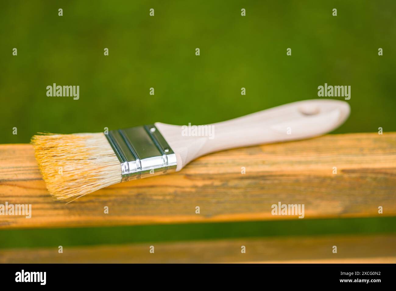 Pinsel auf einer Holzbank mit einem unscharfen grünen Grashintergrund. Der Pinsel hat einen Holzgriff und einen Pinsel aus Naturborsten. Stockfoto
