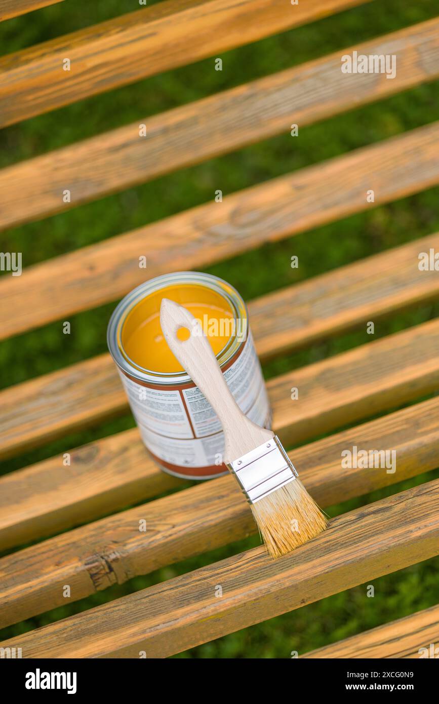 Pinsel und Dose Farbe auf einer Holzbank im Freien öffnen. Die Farbe ist goldgelb und die Bank ist aus natürlichem Holz. Stockfoto