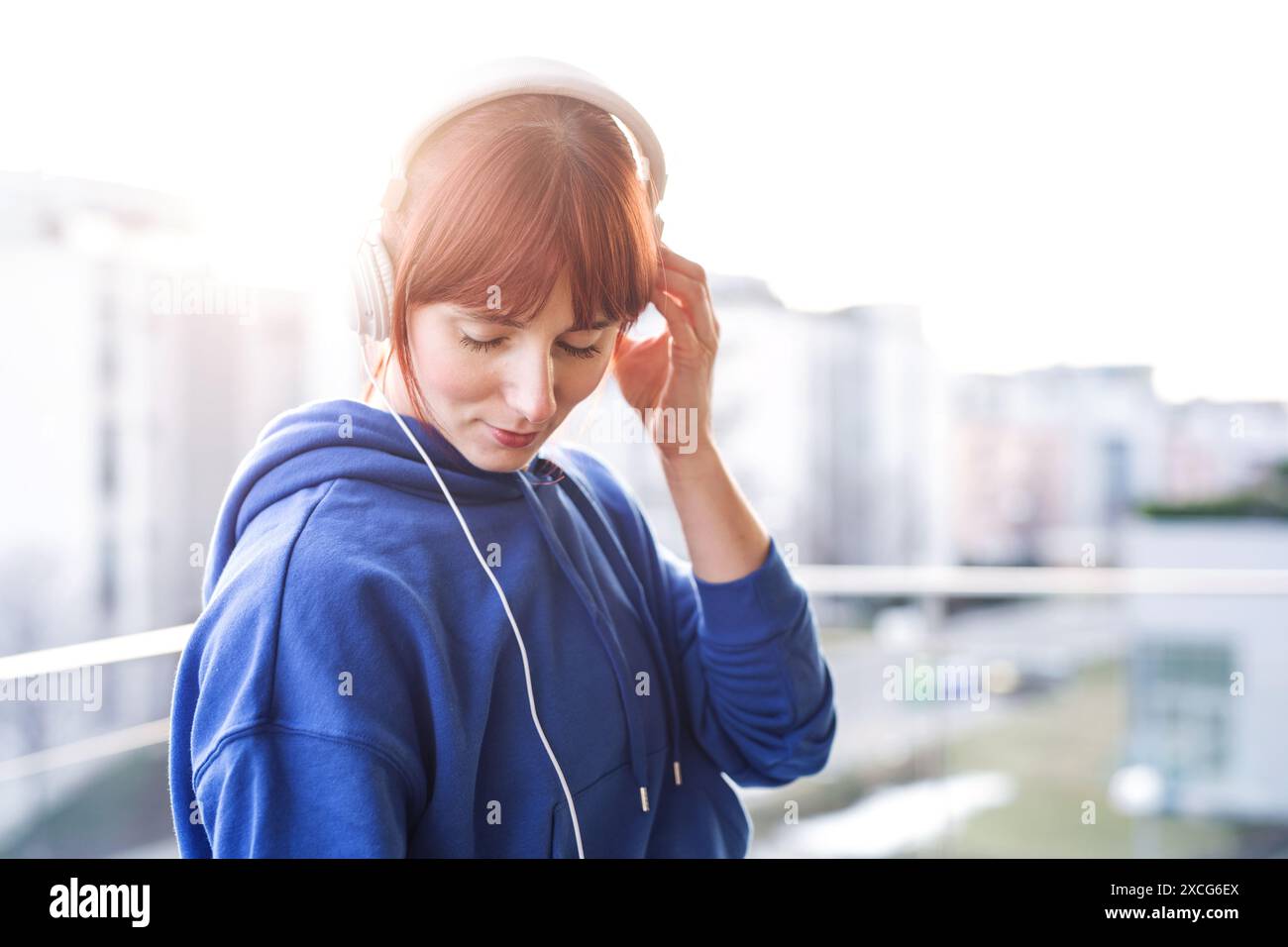 Schöne rothaarige Frau nach einer Fitness-Routine, auf dem Balkon stehend, Musik hörend. Heimtraining, sportliche Frau in Sportbekleidung. Stockfoto