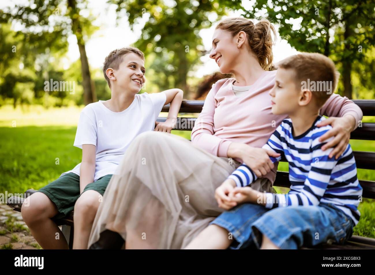 Glückliche Mutter sitzt mit ihren Söhnen auf der Bank im Park. Sie haben Spaß zusammen. Stockfoto