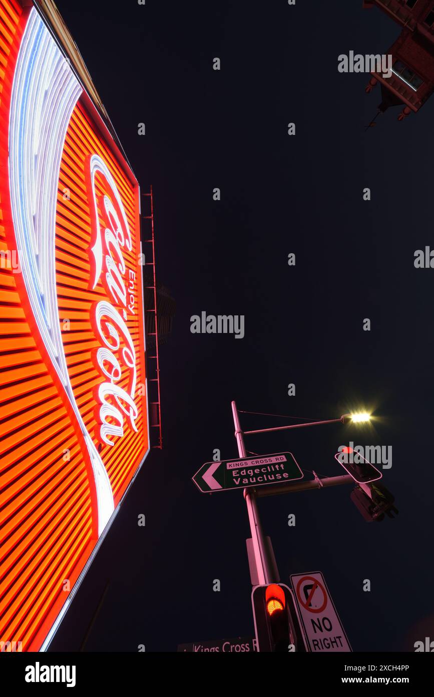 Blick auf das Kings Cross Coke Schild Sydney, beleuchtet in der Abenddämmerung in klarem Abendlicht, Straßenschilder, das KX Hotel und die rote Plakatwand. Stockfoto