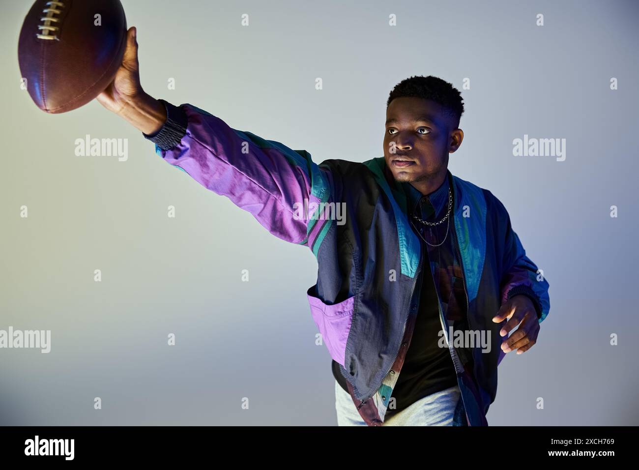 Junger afroamerikanischer Mann in stylischer lila Jacke hält einen Fußball. Stockfoto