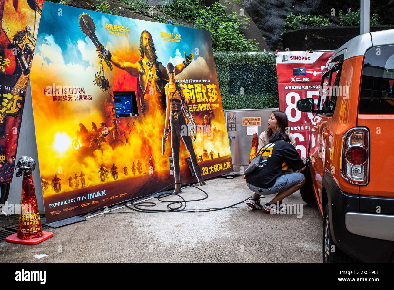 Hongkong, China. Juni 2024. Zwei Kunden füllen ihre Reifen neben einem Filmposter an einer Tankstelle in Quarry Bay im Rahmen einer Werbeaktion zwischen SINOPEC und Warner Bros. Mit Luft Für Furiosa: A Mad Max Saga, basierend auf einer postapokalyptischen Geschichte, in der Benzin eine endliche Ressource ist und Tyrannen im Ödland mit modifizierten Fahrzeugen kämpfen, ist das Tie-in eine einzigartige Marketingstrategie für beide Parteien. (Credit Image: © Ben Marans/SOPA Images via ZUMA Press Wire) NUR REDAKTIONELLE VERWENDUNG! Nicht für kommerzielle ZWECKE! Stockfoto