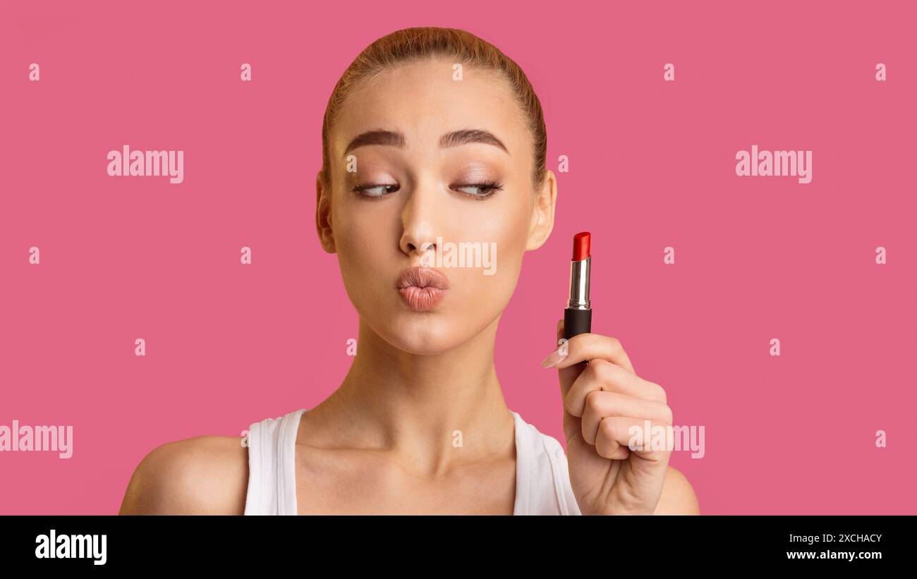 Junge Frau, Die Roten Lippenstift Vor Rosa Hintergrund Aufträgt Stockfoto