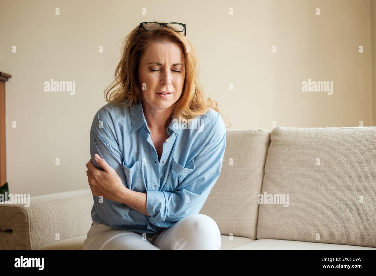 Eine rothaarige Frau in ihren frühen 40ern leidet unter unsichtbaren Schmerzen. Das Bild mit natürlichem Licht zeigt die schwächende Natur verborgener Schmerzen Stockfoto