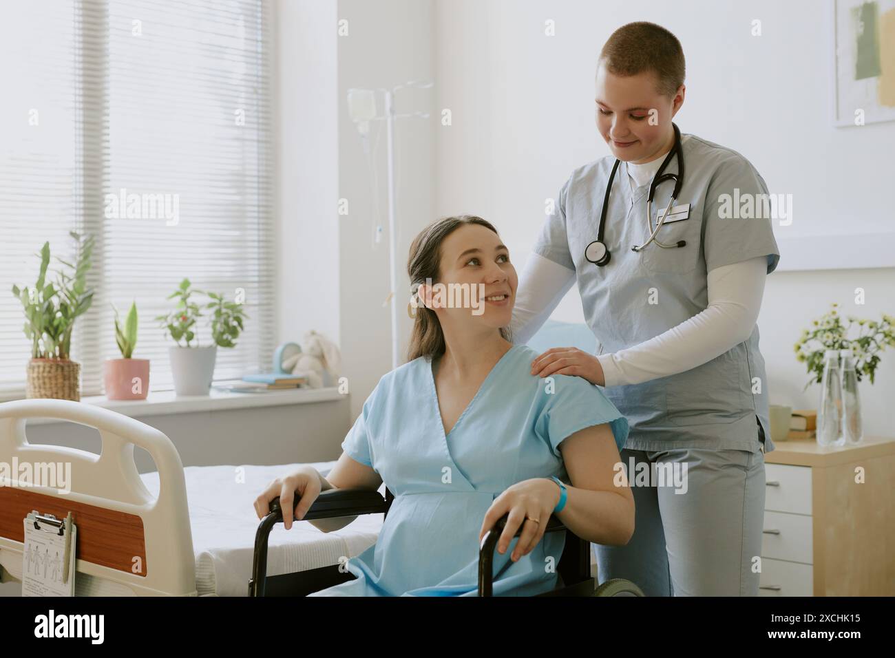 Schwester tröstet schwangere Patientin, während sie im Rollstuhl sitzt und sich auf die Geburt vorbereitet Stockfoto