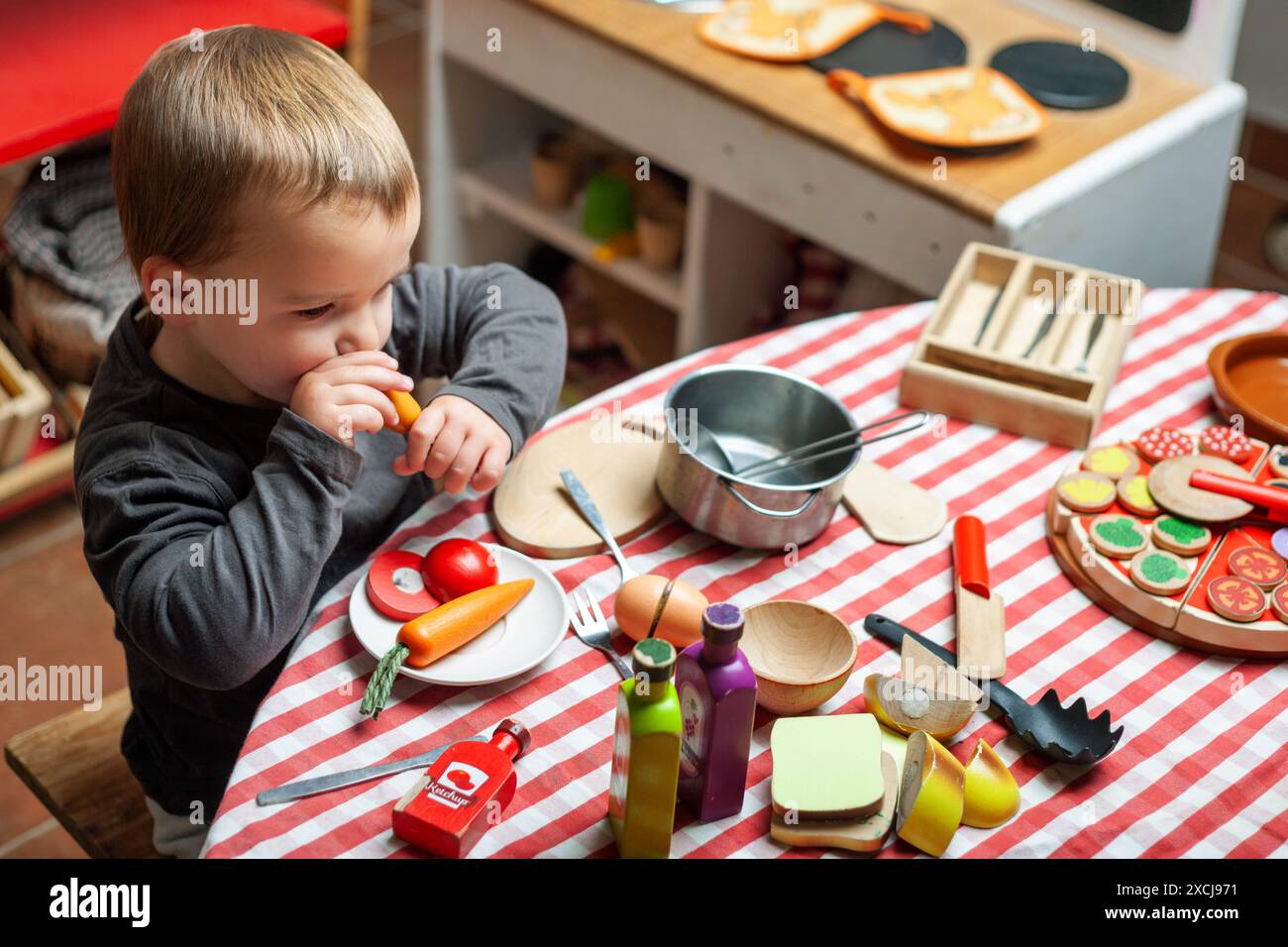 Ein Kleinkind spielt beim Essen im Spielzimmer. Holzspielzeug, symbolisches Spiel. Stockfoto