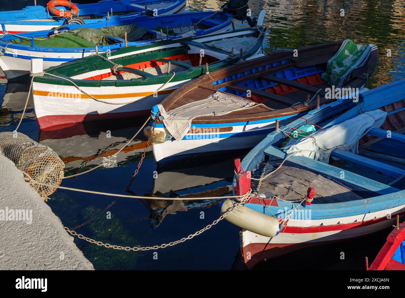 Eine Gruppe traditioneller hölzerner Fischerboote ankert in einem Hafen, in leuchtenden Farben und reflektiert auf dem Wasser. Ideal für Küstenleben und Ma Stockfoto