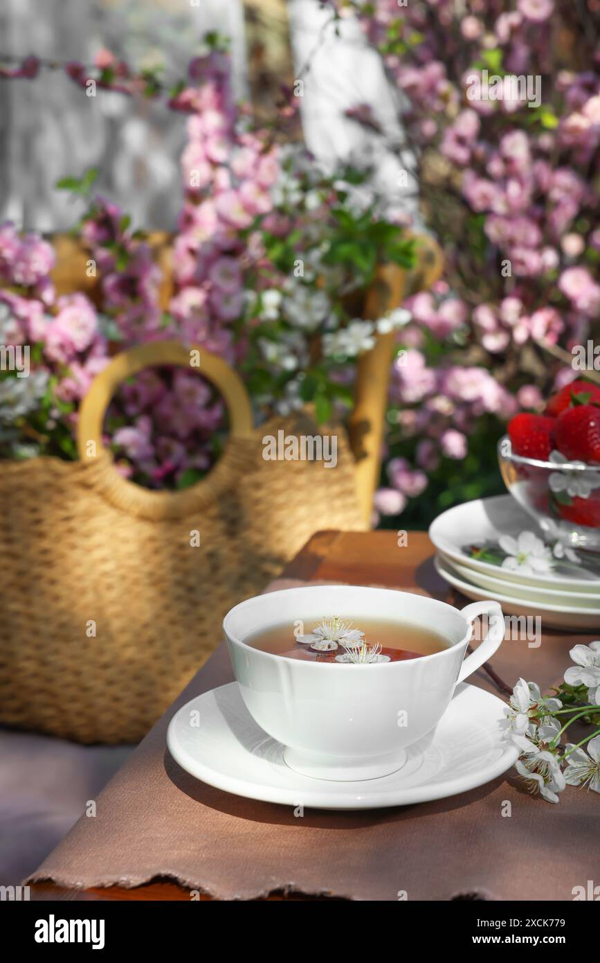 Wunderschöne Frühlingsblumen und reife Erdbeeren auf dem Tisch, die zum Teetrinken im Garten serviert werden Stockfoto