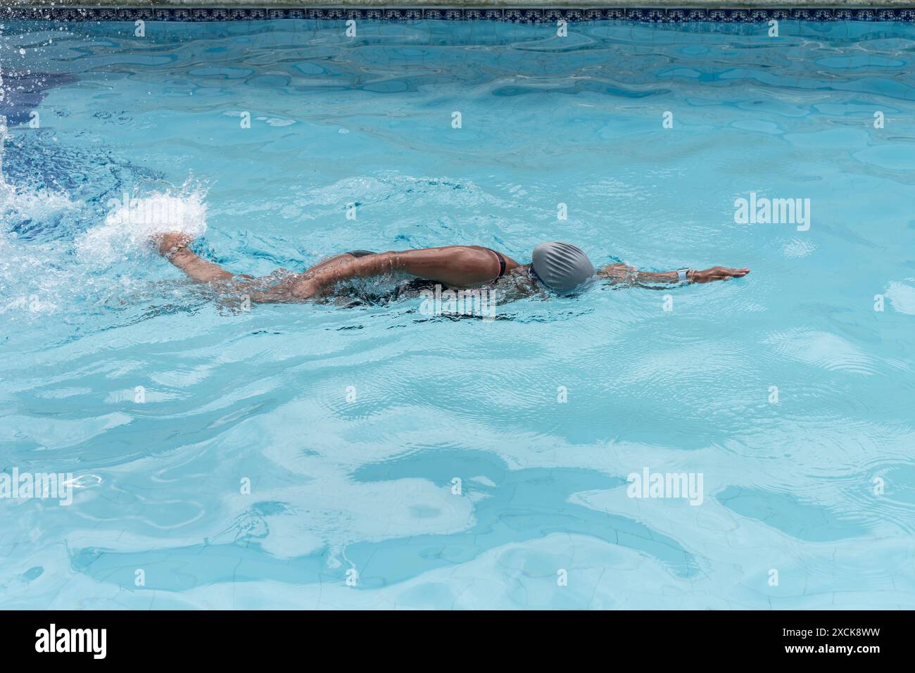 Frau schwimmt in einem klaren blauen Pool, mit Badekappe und schwarzem Badeanzug. Stockfoto