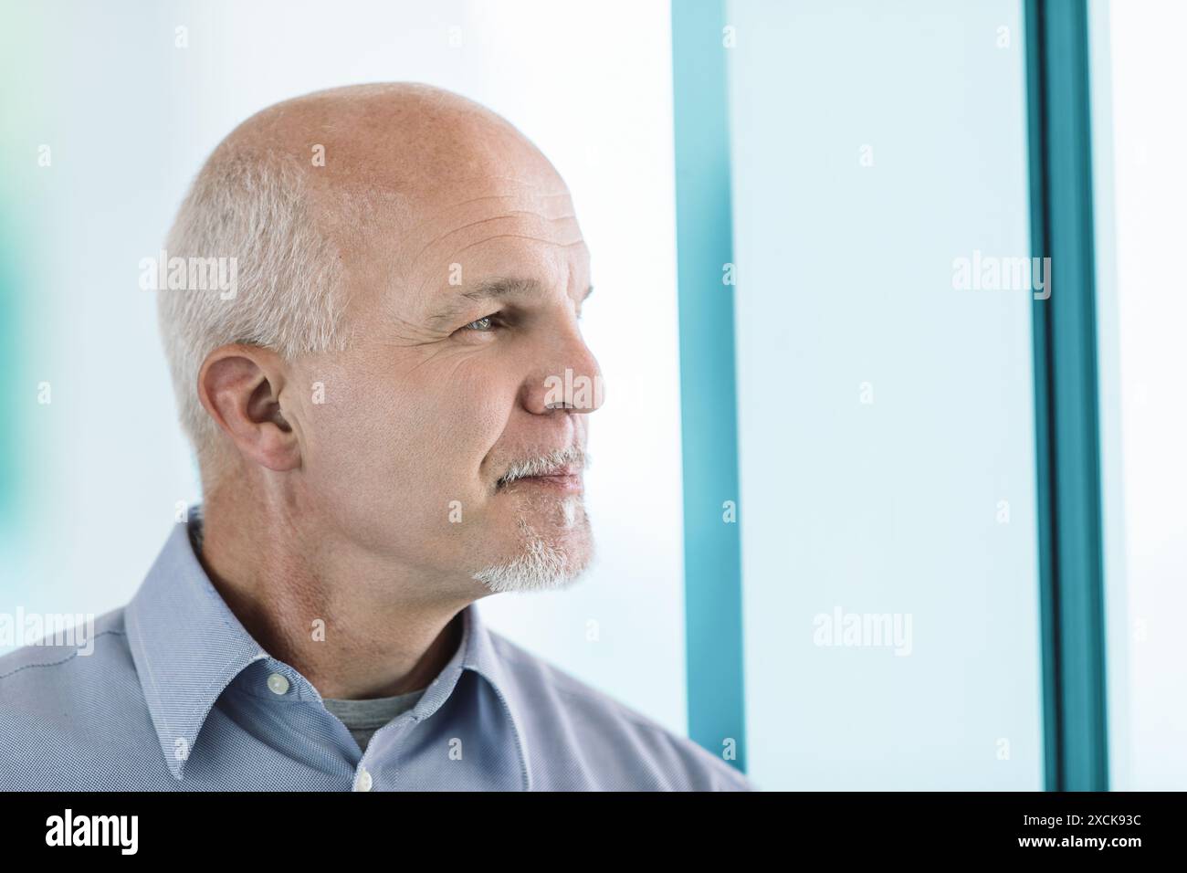 Geschäftsmann denkt und blickt aus dem Bürofenster, denkt mit Entschlossenheit und Zuversicht über zukünftige Entscheidungen, umgeben von Blautönen Stockfoto