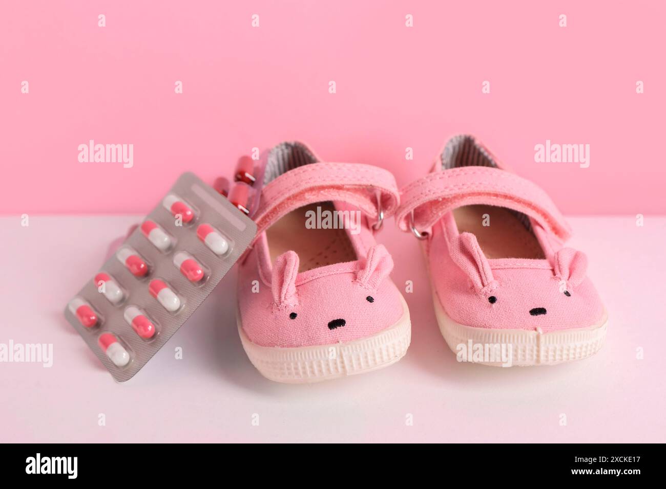 Niedliche Babyschuhe und Pillen auf farbigem Hintergrund Stockfoto