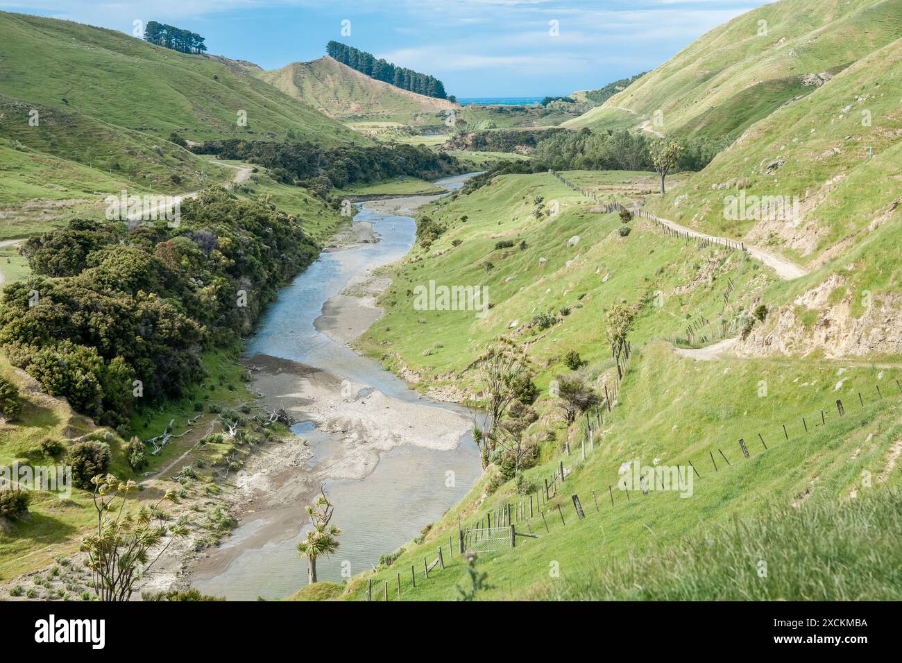 Feldweg und Zaunlinie entlang des Hügels entlang des Flusses unterhalb des Tals der neuseeländischen Farm. Stockfoto