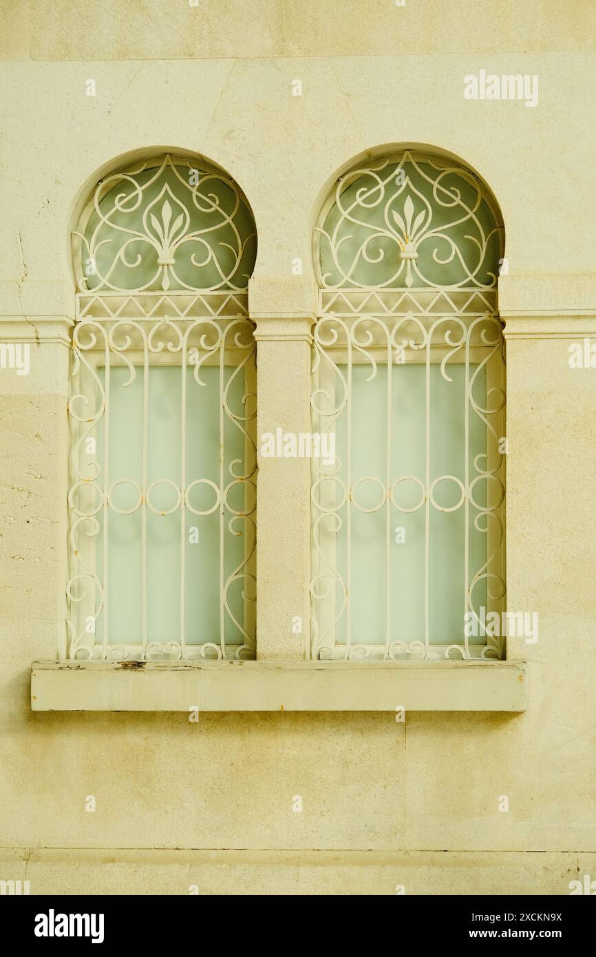 Zwei Fenster mit einem weißen Rahmen und einem grünen Vorhang. Die Fenster sind gewölbt und haben ein dekoratives Design Stockfoto