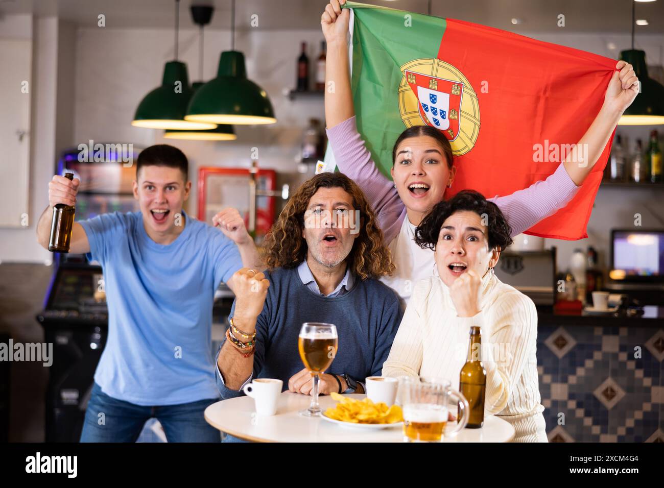Gesellschaft von schreienden jungen erwachsenen Sportfans, die die Flagge Portugals schwenken und die Nationalmannschaft mit Bier im Pub unterstützen Stockfoto